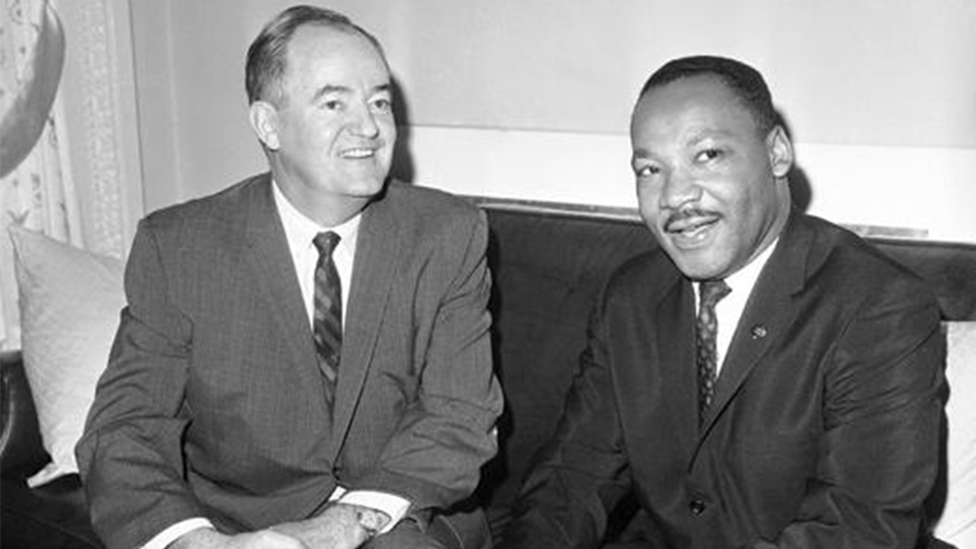 Hubert H. Humphrey and Martin Luther King Jr. sit together and smile at someone off-camera