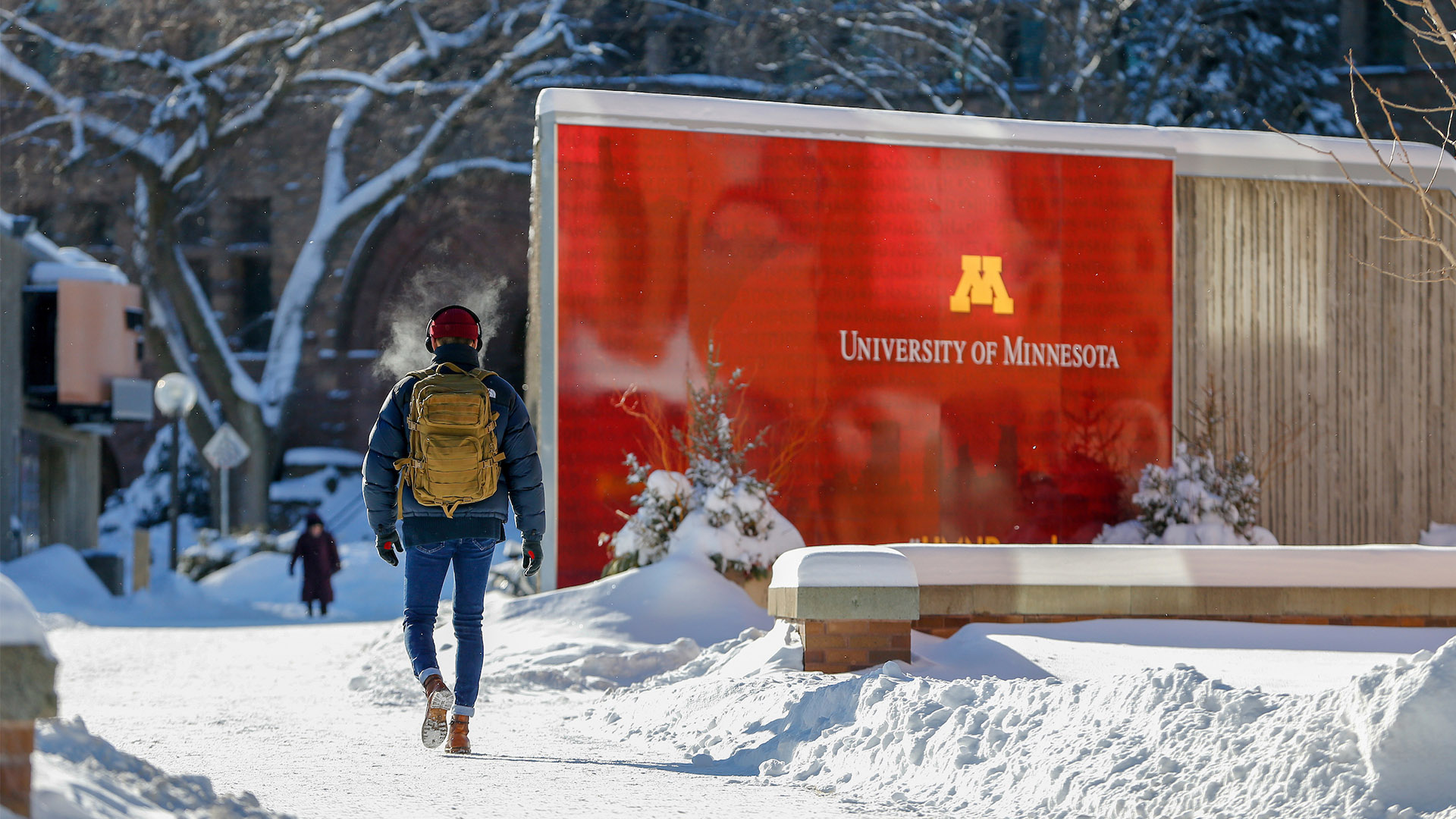 A student walks past a U of M sign on a snowy campus