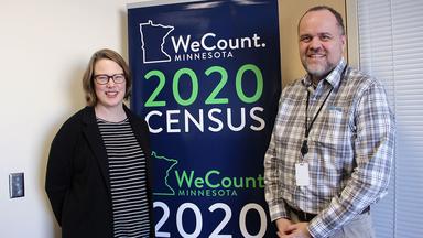 Alumni Susan Brower and Andrew Virden stand near a Census poster